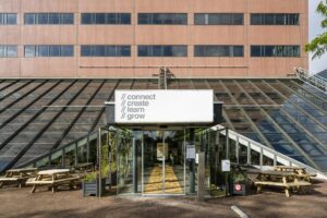 Ingang van een modern kantoorgebouw aan de Johan Huizingalaan met glazen gevel en de woorden "connect, create, learn, grow" op een bord.
